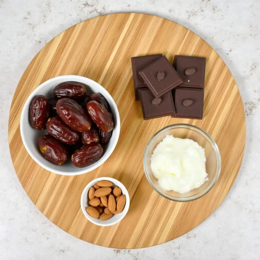 Fresh Medjool dates, raw almonds, dark chocolate, and coconut oil on a wooden board